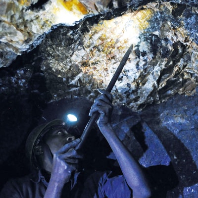 A miner at work in a dark mine, where part of the space is lit up by the light on the miner's helmet